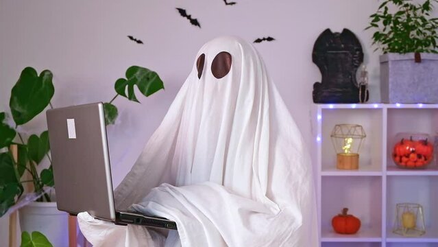 The ghost of Halloween uses a laptop to surf the Internet, to browse online stores, markets. A ghost makes an order computer for Halloween. The ghost pays for an online purchase. Neon light.