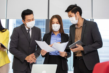 Asian corporate team wearing medical face mask brainstorming, discussing and sharing idea of new project at office. new normal working and social distancing during Coronavirus epidemic concept