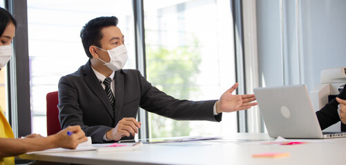 Asian male manager wearing medical mask discussing work at the meeting in the office conference room with team.