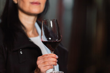 Woman in the wine cellar with barrels in background drinking and tasting wine.