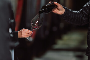 Man pouring fine red wine into a woman glass during a tasting in a wine cellar, close up