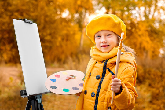 Autumn Baby Girl Drawing in Fall Leaves Park, Little Kid Painting, Children Creativity. little girl artist with a brush and paints in her hands in autumn in the park draws a landscape with leaves