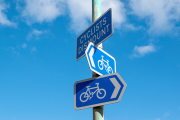 Cyclists dismount sign with blue cycle path signs pointing in opposite directions. Set against a blue sky. Editorial bicycle content. Information signage for a cycle route. Cycle safety