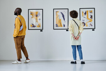 Rear view of young people looking at paintings on the wall at art gallery - obrazy, fototapety, plakaty