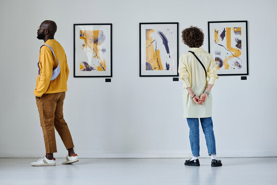 Rear view of young people looking at paintings on the wall at art gallery