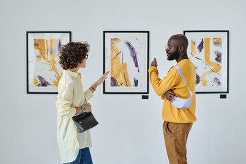 Young people discussing art together standing against the pictures at gallery