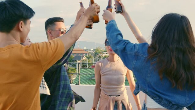     ..Group of young Asian people enjoying with friends together, holding beer bottle and dancing on rooftop party at sunset..