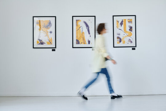 Blurred motion of young woman walking along art gallery with modern art on the wall