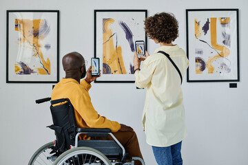 Rear view of young couple making photo of modern art on their mobile phones at gallery