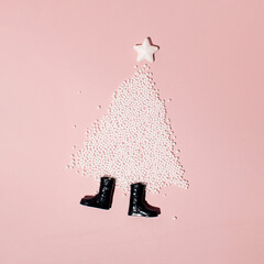 Christmas tree shape, white star on top and pair of boots, creative winter inspired layout against pastel pink background. Merry Christmas and Happy New Year greeting card idea. 