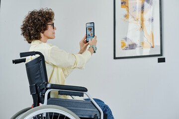 Young woman with disability making photo of modern art on her mobile phone
