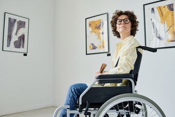 Young girl with disability sitting in wheelchair and enjoying modern art