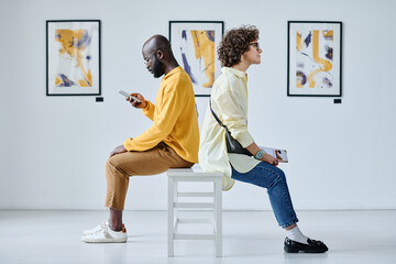 Young couple sitting on chair back to back and resting after excursion at art gallery