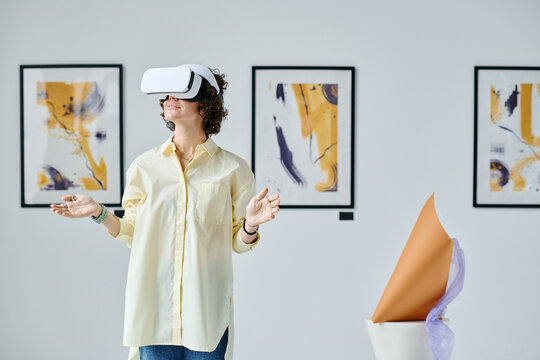 Young woman using virtual reality glasses standing at gallery of modern art during exhibition