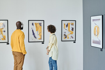 Young people examining modern art on the wall during exhibition at art gallery