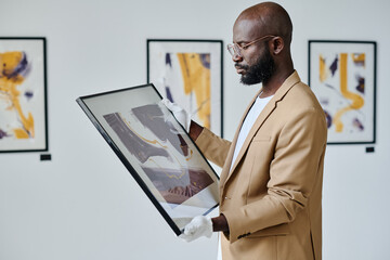 African guide examining modern art in his hands while working at art gallery - obrazy, fototapety, plakaty