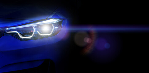 Car headlights with light rays and copy space, banner. Neon light of car headlights on a dark background with lens flare, panorama, close up .