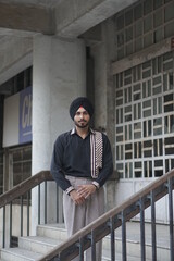 man with black turban and shirt posing infront of building