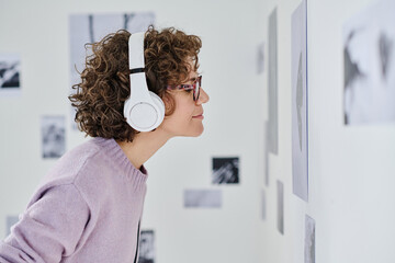 Side view of young girl listening to guide in headphones while watching photos on wall at gallery