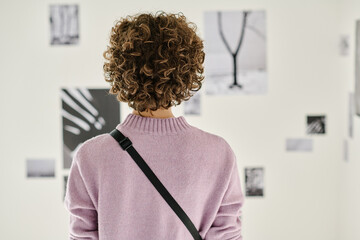Rear view of young visitor standing at art gallery and enjoying modern art