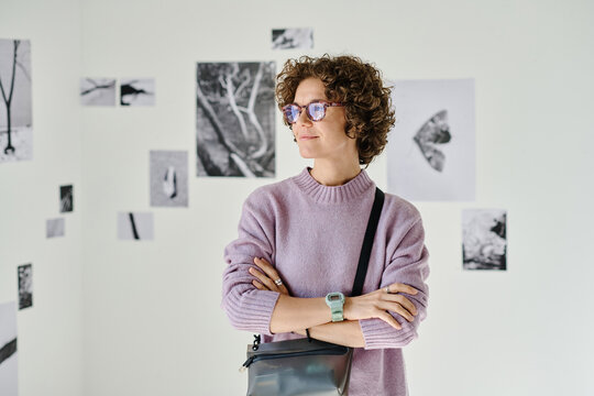 Young woman in eyeglasses standing with her arms crossed at gallery of modern art