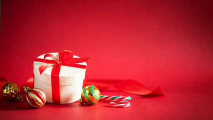 Christmas gift in round box with red ribbon and Christmas ornaments on red background. Stock image with copy space