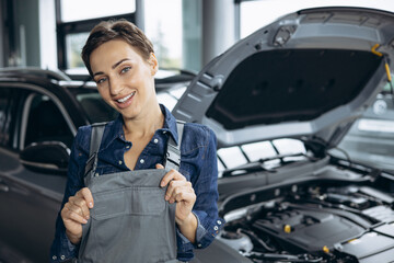 Naklejka na ściany i meble Young woman car mechanic checking car at car service