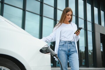 Happy young adult woman smiling wide, looking away, charging automobile battery from small public...