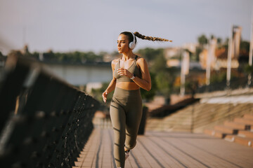 Active young beautiful woman running on the promenade along the riverside - obrazy, fototapety, plakaty