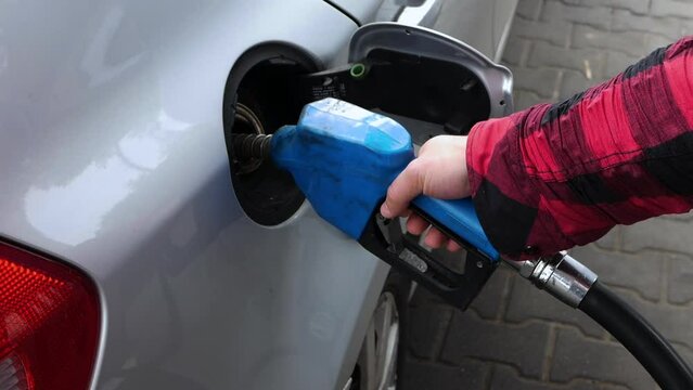 A man refuels a car with gasoline at a gas station, inserting a gasoline hose into the auto tank