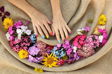 Multicolored manicure and pedicure with a variety of flowers on a background of burlap.
