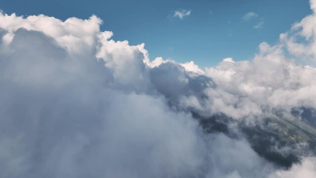 Mountains are seen flying through the clouds below. Air flight through low cloud cover. Weather change, global warming. aerial view