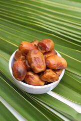 Organic Date Palm Fruit or Phoenix Dactylifera in a Bowl Isolated on Palm Leaf in Vertical Orientation