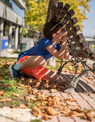 Boy playing hide and seek. Looking through a gap in a wooden park bench