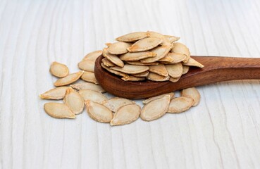 Dry Pumpkin Seeds in a Wooden Spoon Isolated on White Wooden Background
