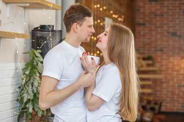 Loving couple kisses each other, standing in morning in kitchen at home and drinking coffee.