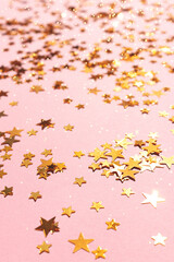 Fototapeta na wymiar Shiny golden stars confetti scattered on a pink background. Selective focus.