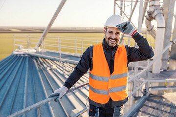 A happy industry worker is greeting while leaning on the railing and smiling at the camera.
