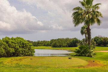 Beautiful view of nature landscape with golf course spot in front of little pond. Green bushes and pale blue sky on background. Aruba. 