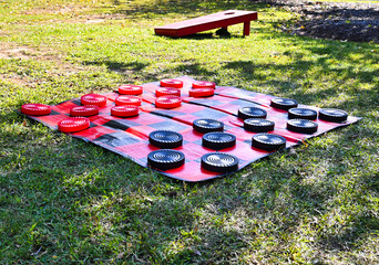 A view of a giant checkerboard with red and black checkers on the grass at a park.