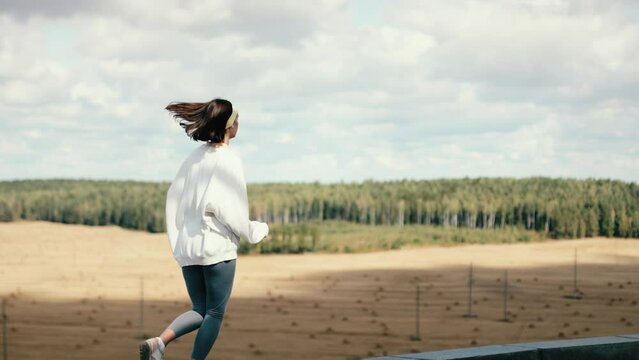 Beautiful fitness woman on the top of the hill. Brunette female jogging on the edge. felling joy and freedom. Amazing landscape background.