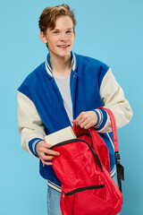 a young student in a bomber jacket takes out a notebook from his backpack looking at the camera
