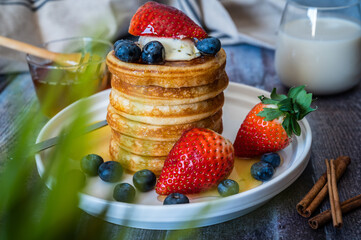 Through the grass view of Stack of pancakes with honey stick, strawberry, blue berry and whip cream on top in plate, delicious dessert with milk