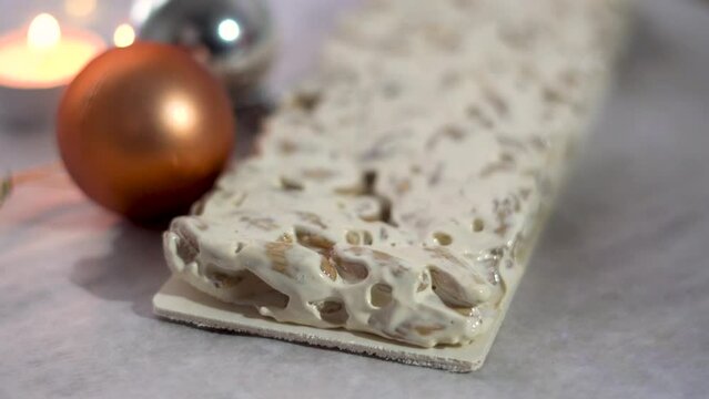 slow motion, side view of a piece of nougat from Alicante, with Christmas decorations in the background.