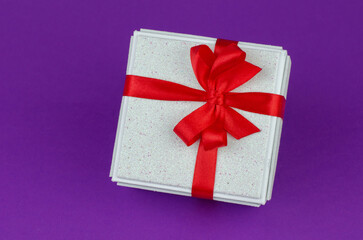 White gift box with red ribbon on purple background