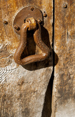 traditional vintage handmade metal door handle on a wooden door at the entrance to a Spanish stone...