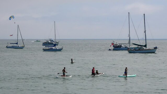 A group of paddle board surfers passing boats that are standing by at the coast of Santa Barbara near Sterans Wharf.