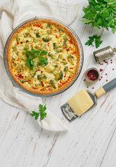Quiche Lorraine with chicken and broccoli on a light wooden background. Pie with vegetables, poultry, cheese, parsley and spices. Traditional French food. Selective focus, top view and copy space