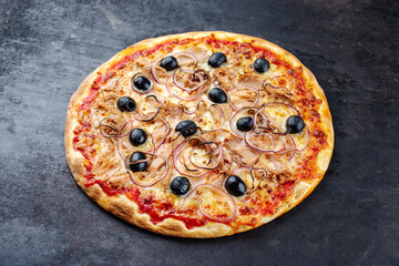 Traditional Italian pizza al tonno with tuna, onion and olives served as close-up on an old rustic board with text free space