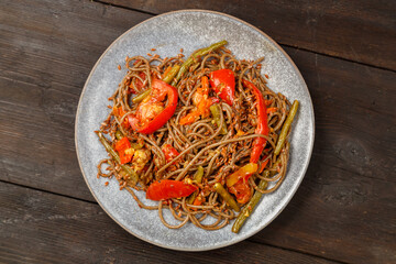Soba with vegetables in soy sauce with spices in a gray plate on a wooden table.